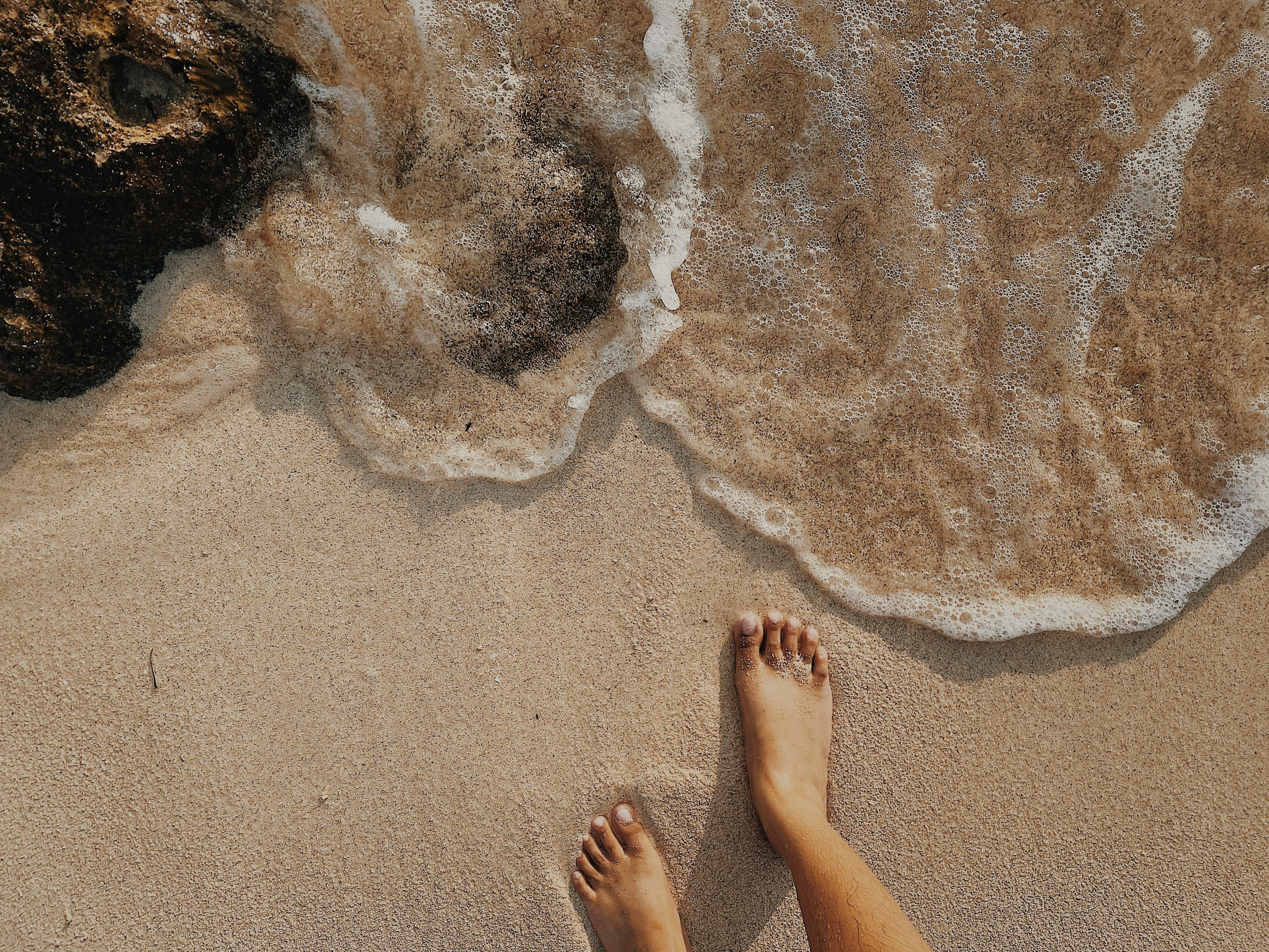 Feet on a sandy New Zealand with waves crashing nearby next to rockpools.