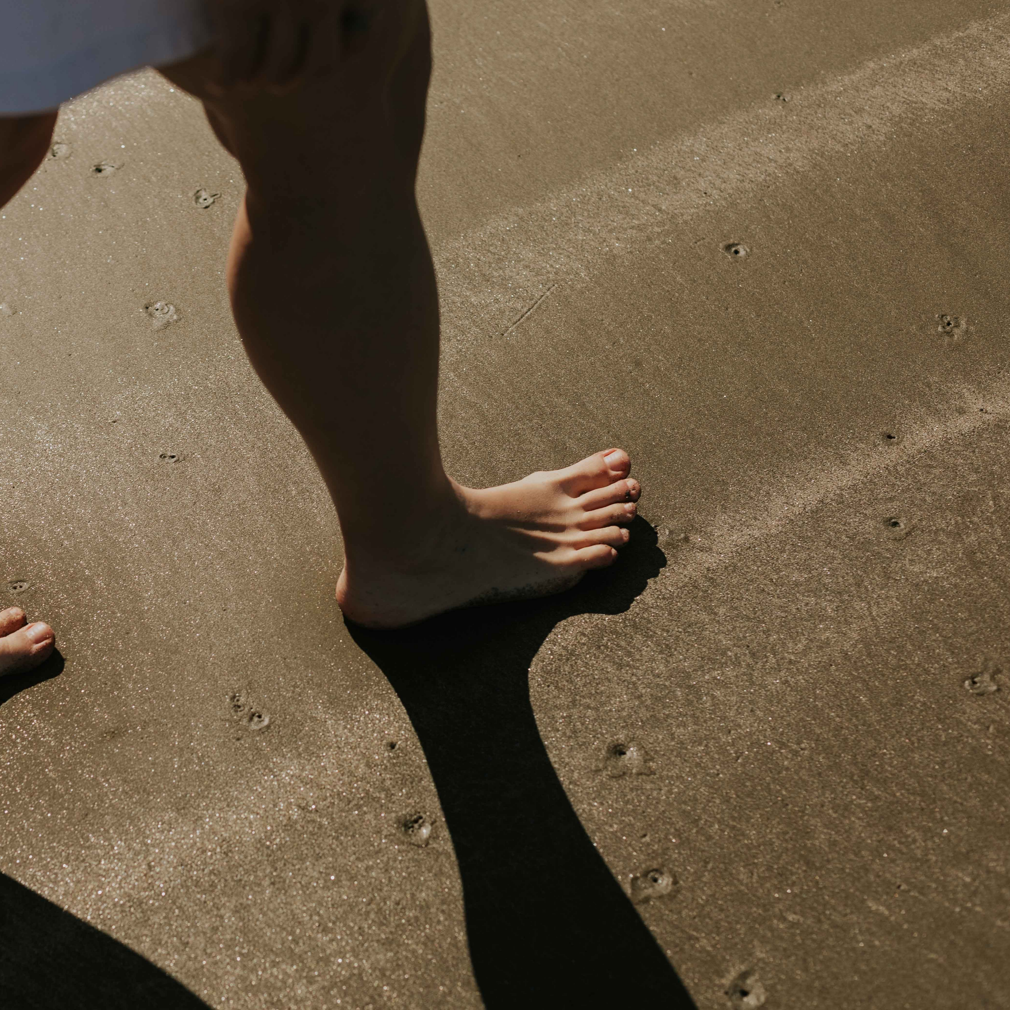 A person walks along the wet sand of a beach in New Zealand.