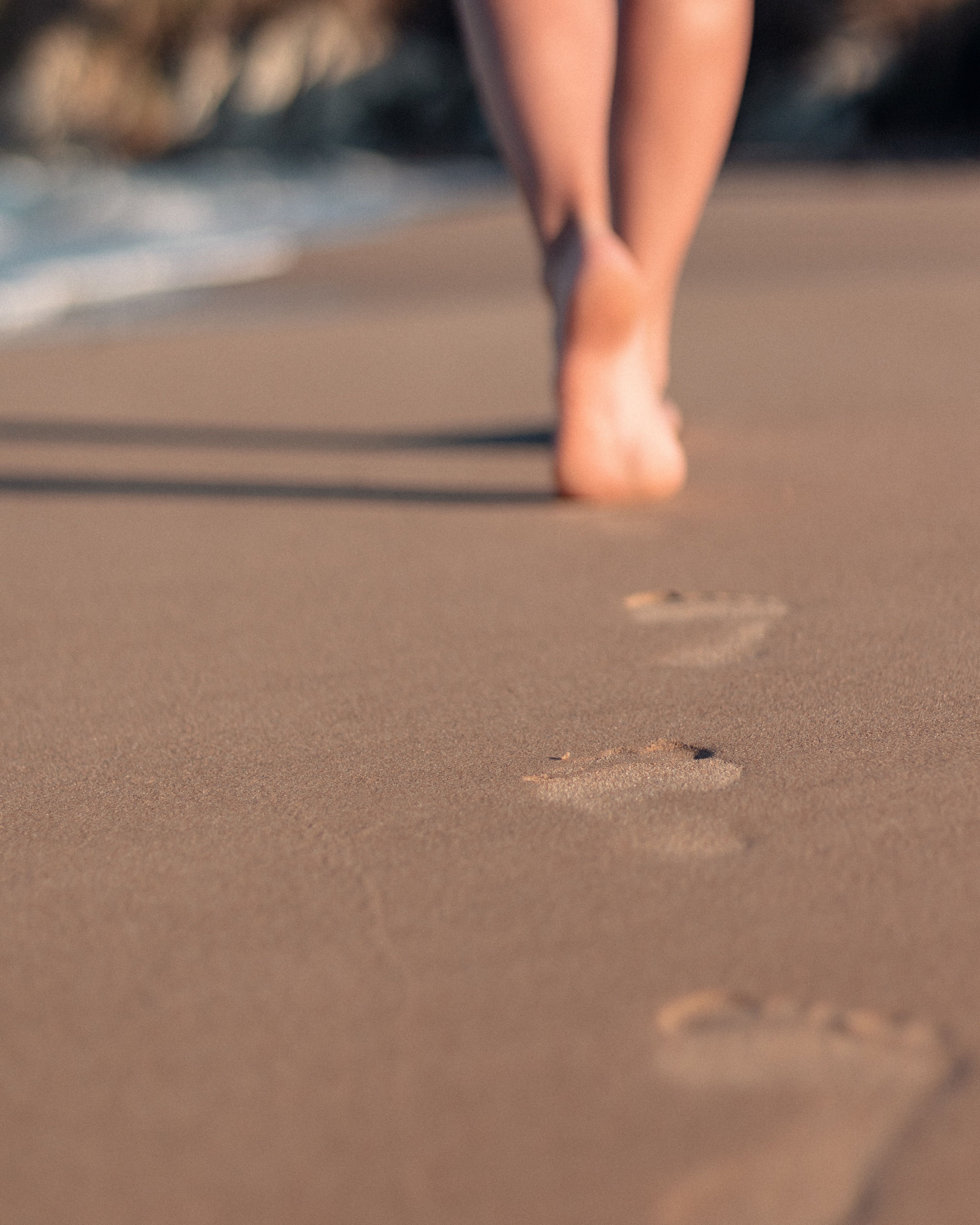 Feet walking on wet sand with ocean waves in the background in New Zealand.